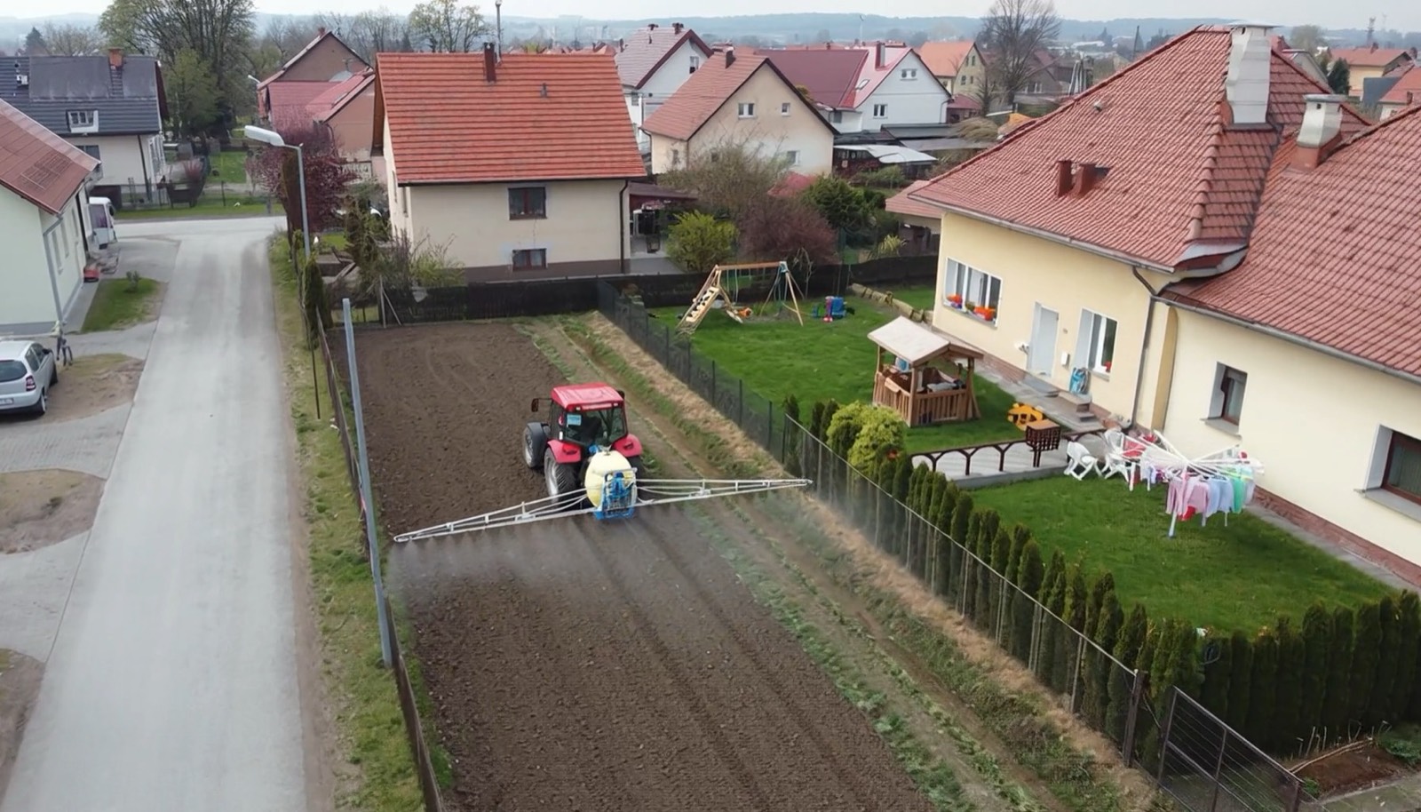 Traktor pracujący na wąskim polu między domami